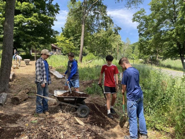 A group of kids shoveling dirt into a wheelbarrow receiving workforce training