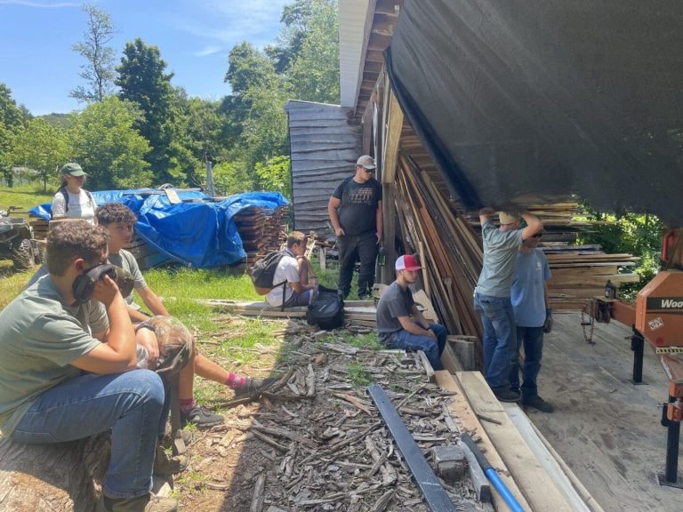 People sitting on the ground outside receiving instruction on a forestry related machine