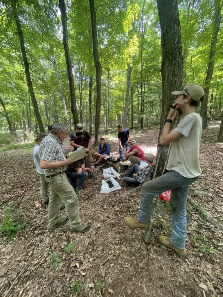 A group in the woods learning workforce skills from the Forestry 101 program