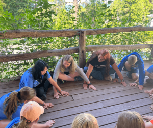 counselors and children siting in a circle on a deck doing a summer camp activity