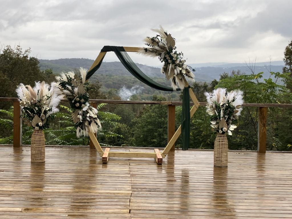 Empty ceremony deck with a pampas grass and floral hexagonal arch overlooking green mountains.